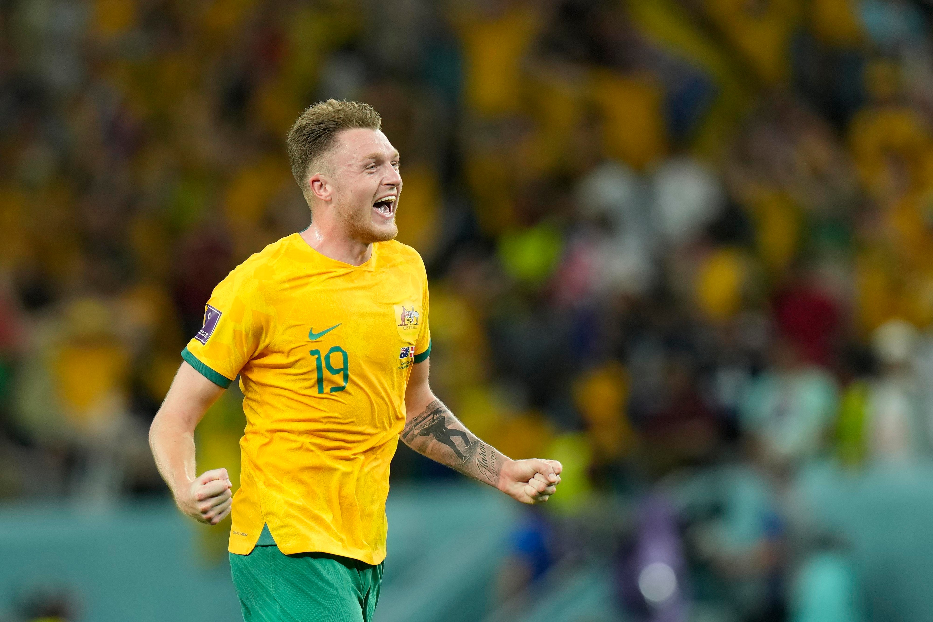 Socceroos player celebrating in a bright gold jersey with both fists clenched